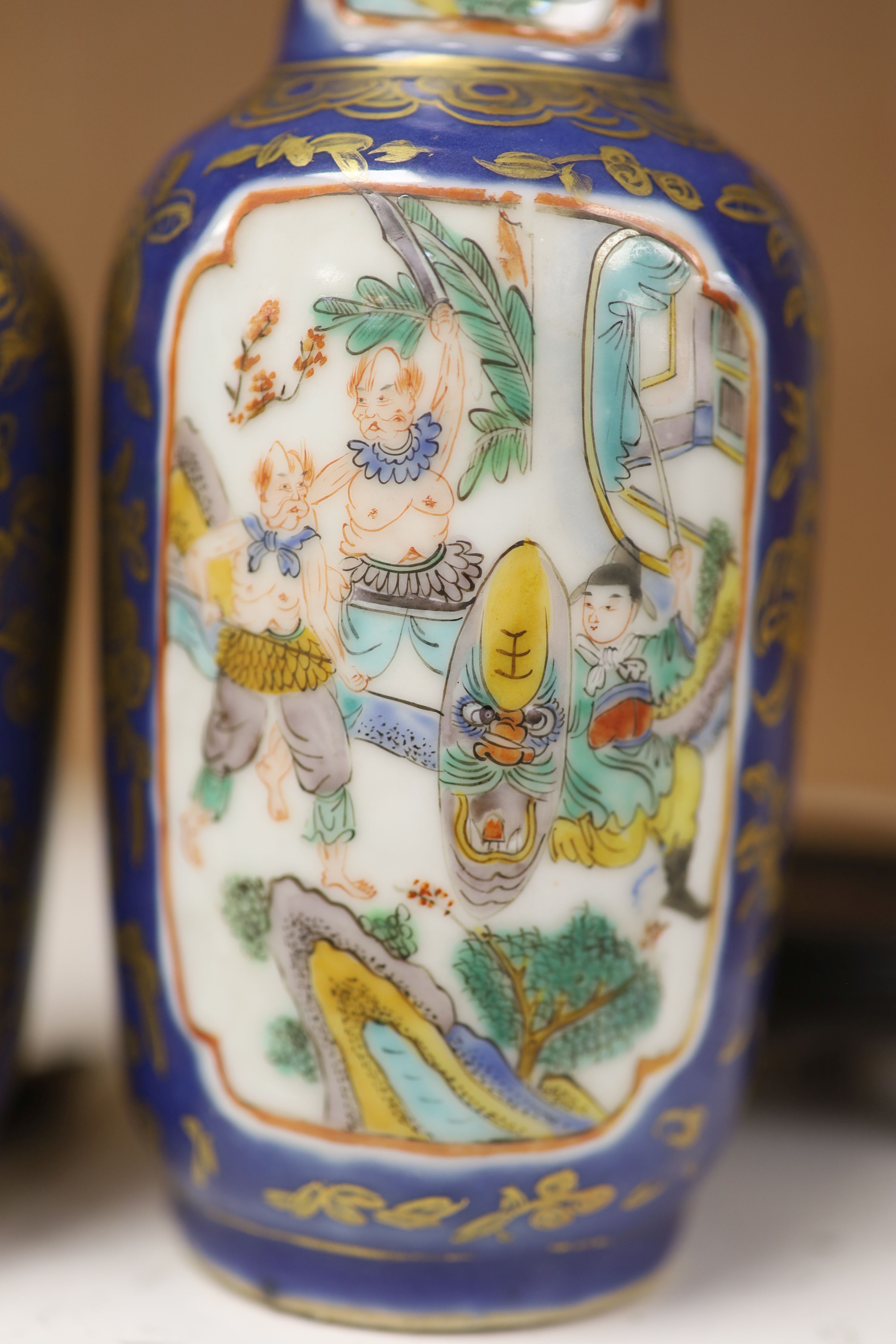 A pair of Chinese Kangxi style blue-ground vases, late 19th century decorated with panels of warriors and heightened in gilt, on carved hardwood stands, height 18cm excluding stand